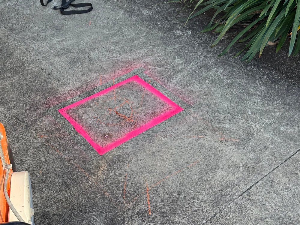 Leak location marked with pink paint on a concrete driveway